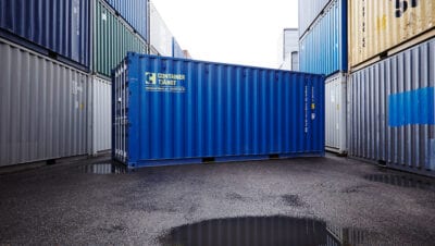 Blå container i dagsljus. Omringad av en containervägg